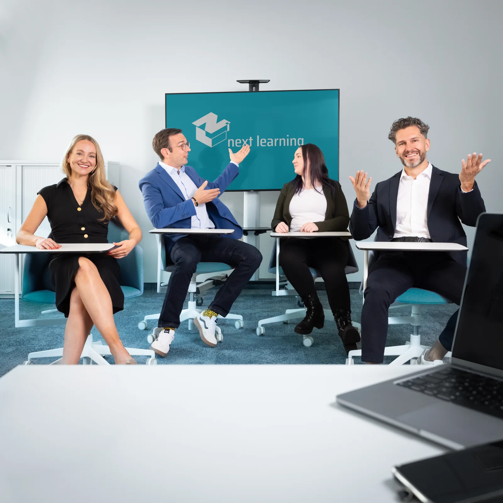 Das Team der next learning im Halbkreis vor dem Bildschirm mit dem Logo der Gesellschaft